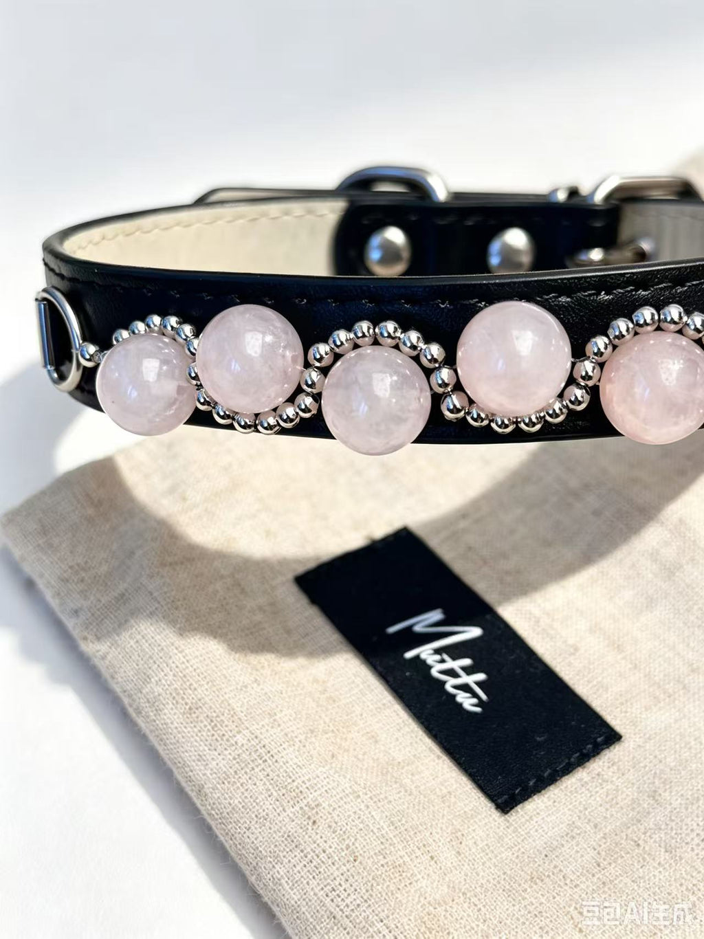 Strawberry pink crystal pet collar resting on Muttu branded linen dust bag, close-up showing rose quartz beads and silver detailing – Muttu